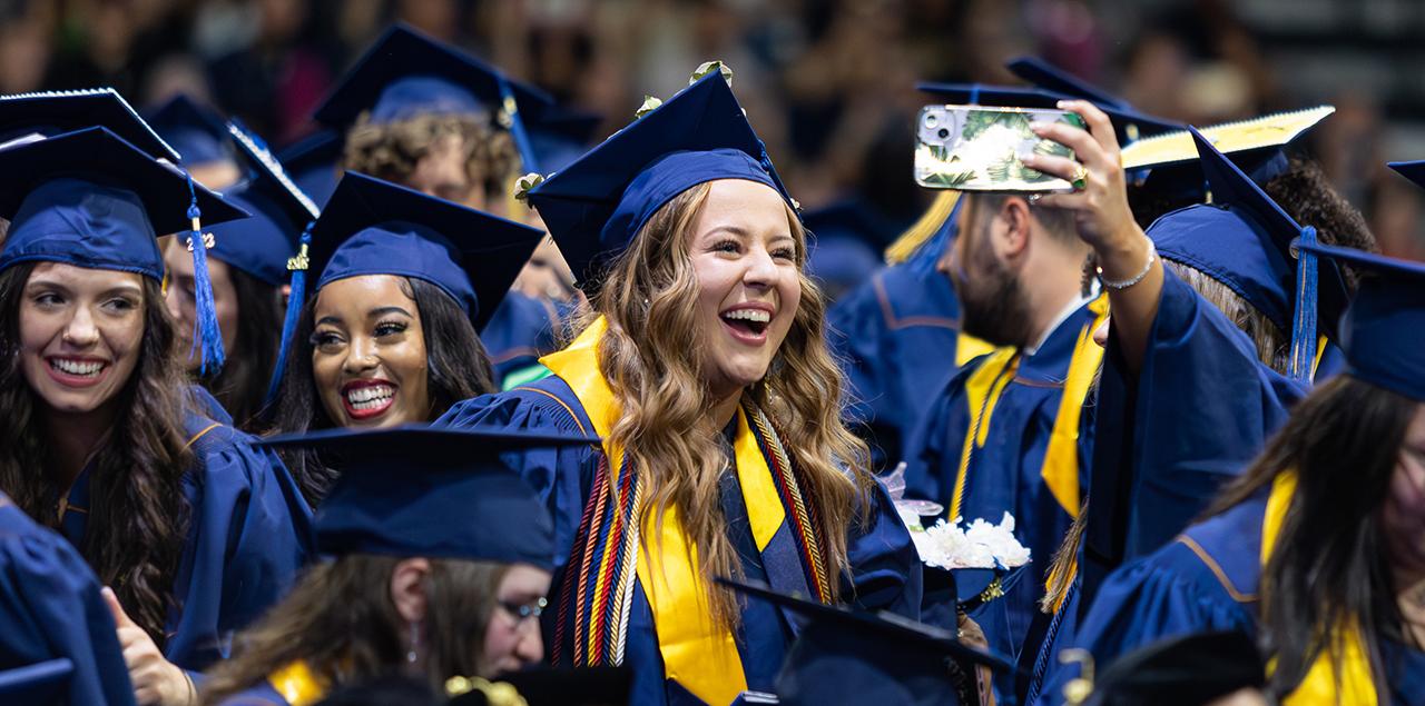 A group of UNC students standing and smiling and taking a selfie in their caps and gowns at graduation