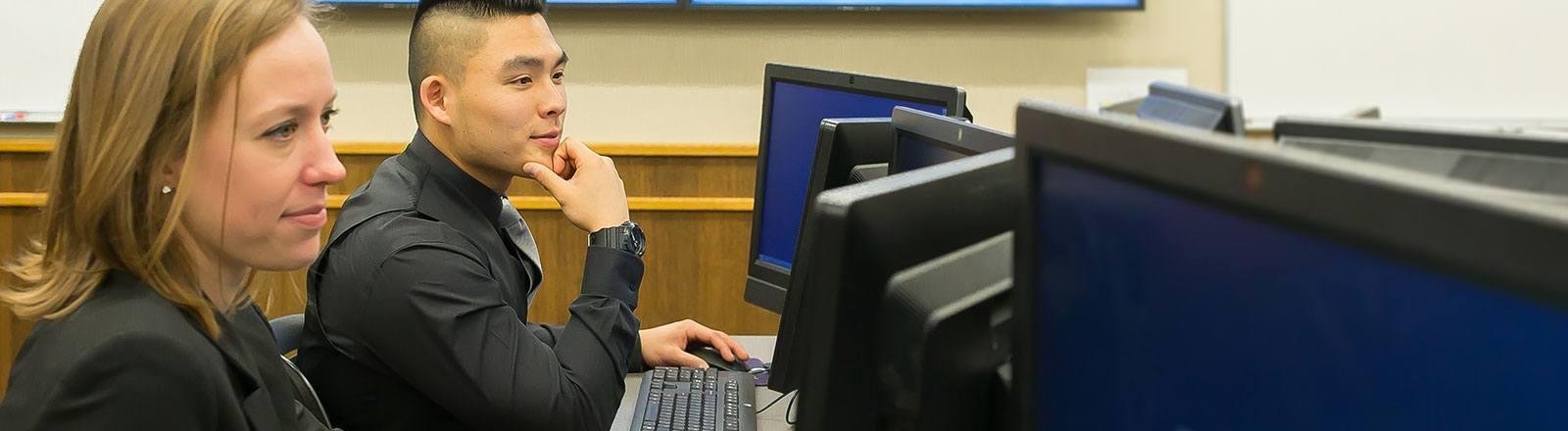 Two business students sitting at desk looking at computer screen